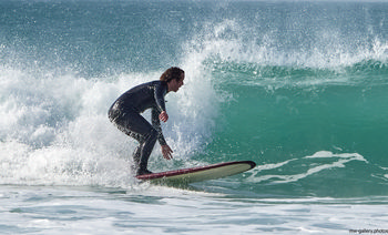 Cornish surfer This landscape photograph was captured on a spring afternoon and features a Cornish surfer riding a wave near the coast at Sennen Cove in Cornwall, United Kingdom. The image shows the surfer, dressed in a wetsuit, skilfully balancing on a surfboard as waves break behind, with the turquoise water and white foam characteristic of this nature-rich beach environment. The ocean is lively with rolling waves, highlighting the popularity of Sennen Cove among surfers and beach visitors in Cornwall. The scene is set along the scenic coast, typical of the rugged beauty found in the United Kingdom, with the natural elements of the beach and the dynamic action of the surfers central to the composition.